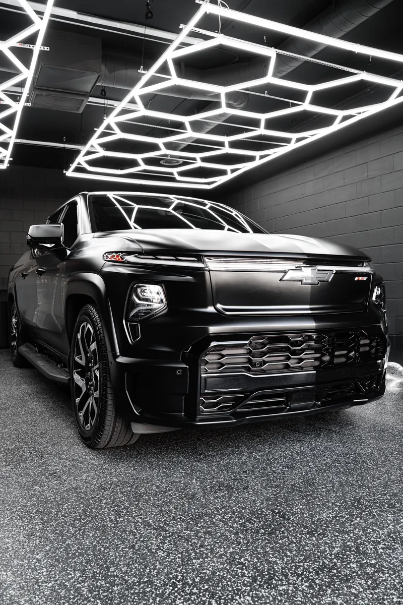 Front of a satin black Chevrolet Silverado EV RST under the hex ceiling lights