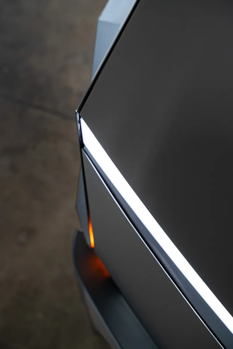 Front corner and light bar edge of a grey-olive Tesla Cybertruck