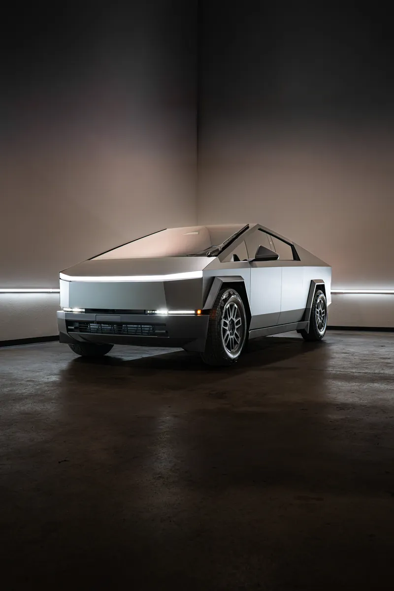 Grey-olive Tesla Cybertruck in a corner of the studio, front three-quarter