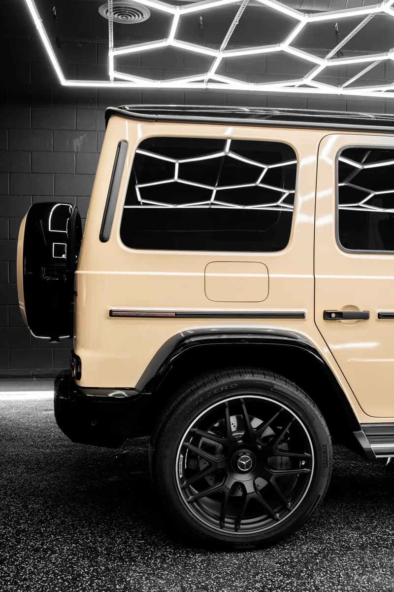 Side of a beige Mercedes-AMG G63 with a gloss black fender flare and black wheel