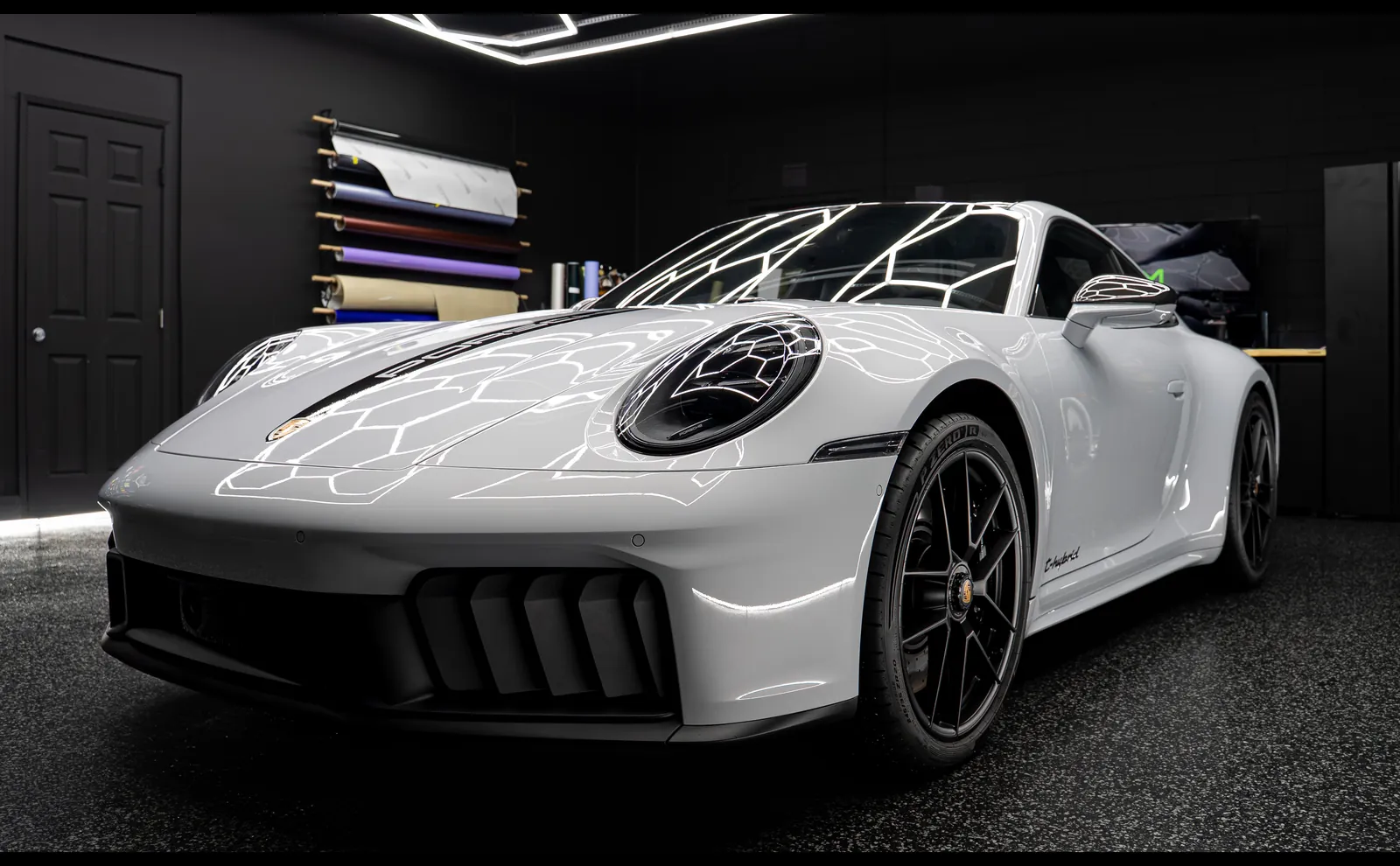 Light grey Porsche 911 Carrera GTS with full body paint protection film, low front three-quarter view in the shop bay