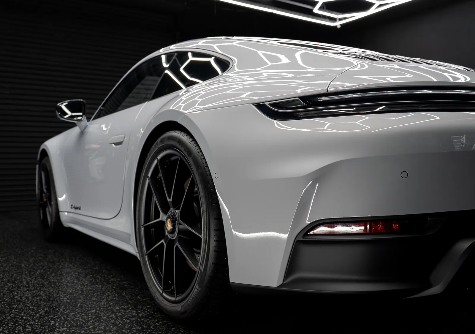Rear three-quarter of a light grey Porsche 911 Carrera GTS with black wheels